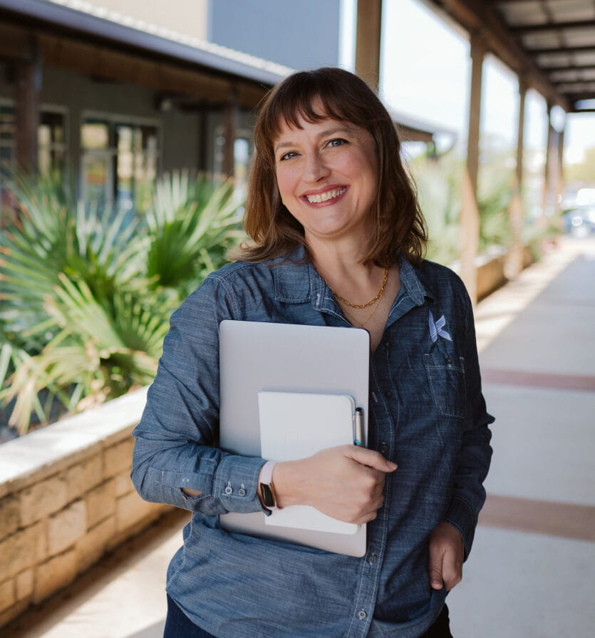 Female agency partner outside holding a closed laptop and notebook while smiling